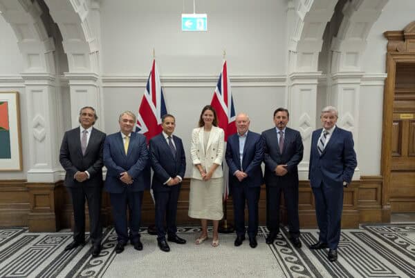 a group of people including UK Minister standing in a room with flags