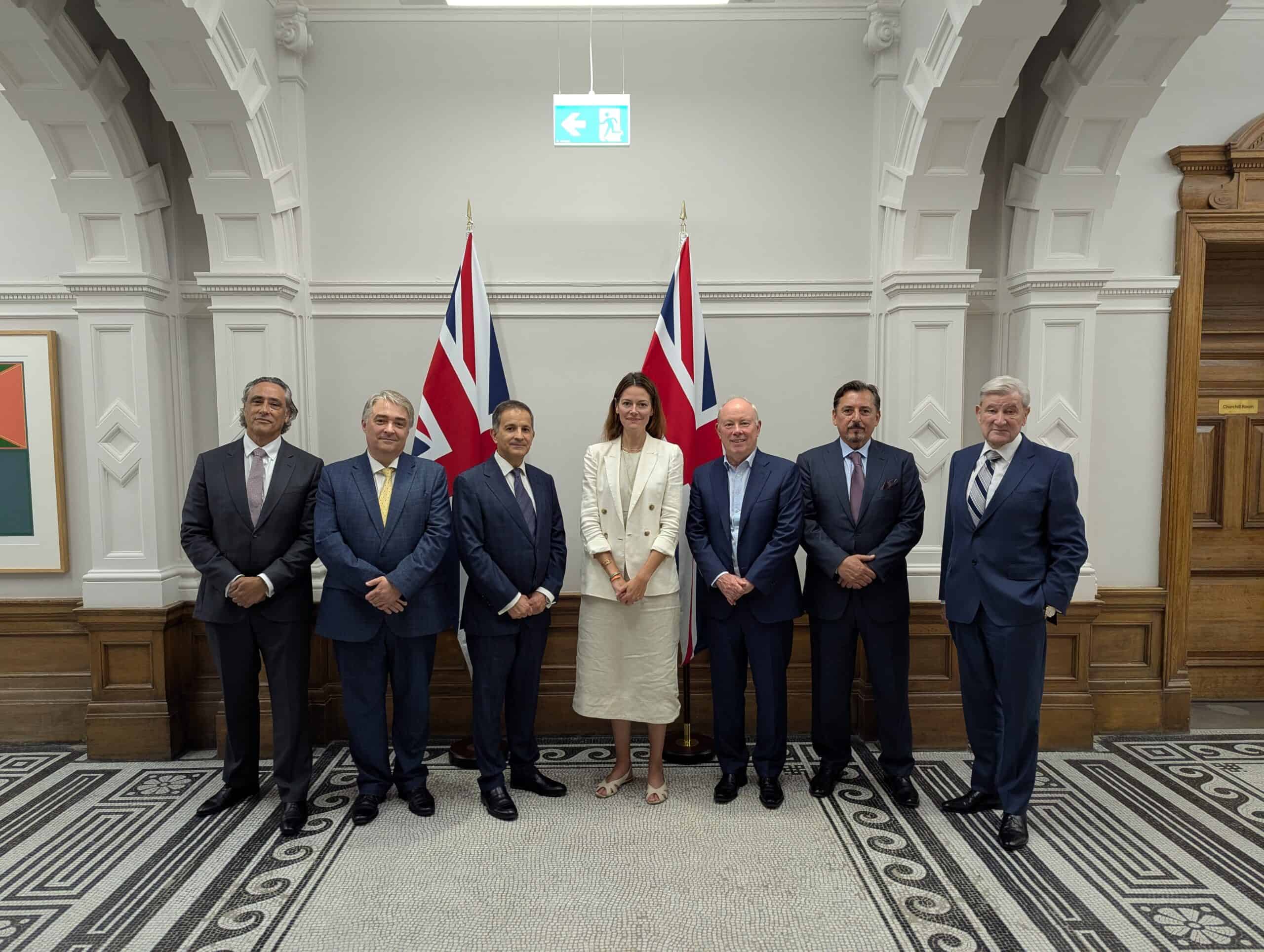 a group of people including UK Minister standing in a room with flags